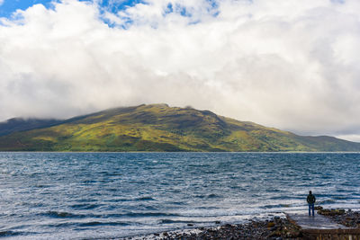 Scenic view of sea by mountain against sky