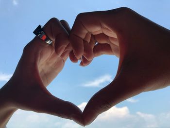 Close-up of hand holding heart shape against sky