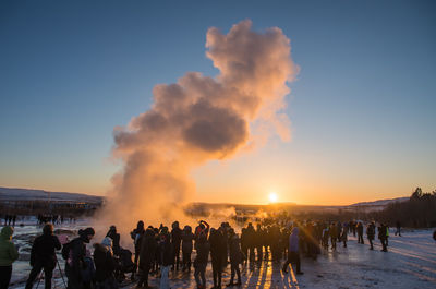 People on volcanic landscape against sky during sunset