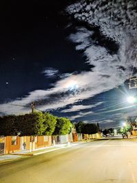 Road by illuminated city against sky at night