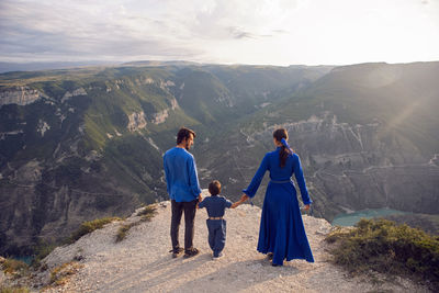 Family of three people stands on the mountain gorge during sunset in dagestan