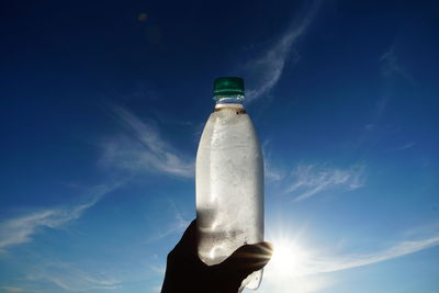 Close-up of hand holding bottle against blue sky