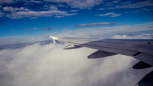 Airplane wing flying over clouds in sky