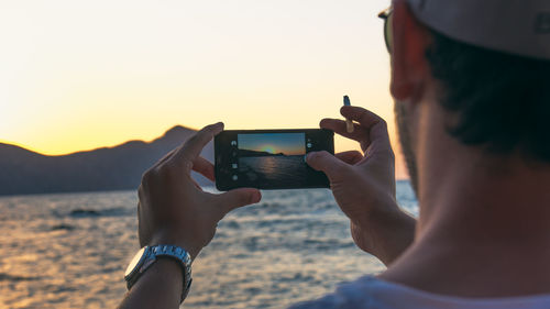 Woman photographing sunset over sea