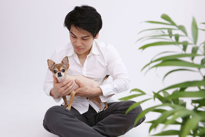 Man with dog sitting by plant against white background