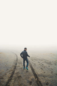 Full length rear view of man walking on sand in foggy weather