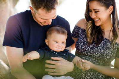 Parents sitting under tree smiling at infant son