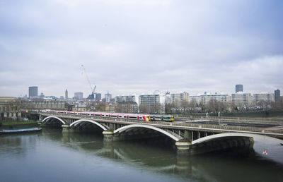 Bridge over river by buildings against sky in city