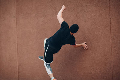 Man with arms raised against wall