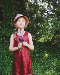 Girl in red dress looking up while standing against trees