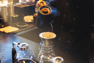 Hand drip coffee, barista pouring hot water on roasted coffee ground with filter in coffee shop.