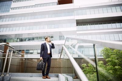 Low angle view of male lawyer talking on smart phone while standing against building