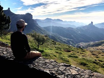 Man sitting on mountain against sky