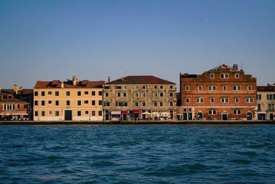 Buildings by sea against clear sky