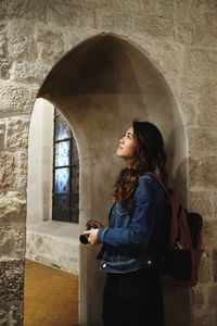 Woman looking away while standing against window