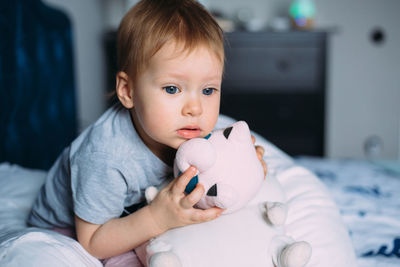 Little child is having fun, playing with soft toys on the couch at home.