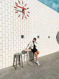 Woman sitting on chair against wall