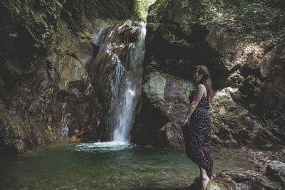 Side view of young woman standing against waterfall