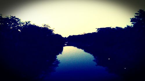 Reflection of silhouette trees in lake against clear sky