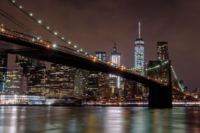 Brooklyn bridge over east river by one world trade center in illuminated city at night