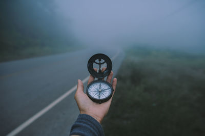 Cropped hand holding navigational compass against sky