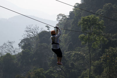 Person on zip line against tree mountains