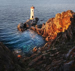 Lighthouse on rock by sea against buildings