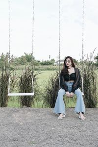 Young woman sitting on swing against sky
