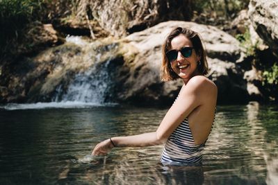 Portrait of young woman wearing sunglasses while standing in lake