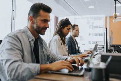 Businesswoman using computer while working amidst male colleagues at desk in office