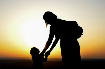 Silhouette woman with arms raised against sky during sunset