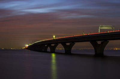 Illuminated bridge over river against sky at night