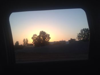 Silhouette trees by road against clear sky during sunset