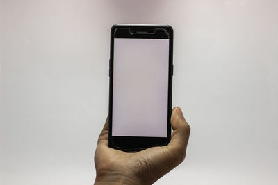 Close-up of hand holding smart phone against white background