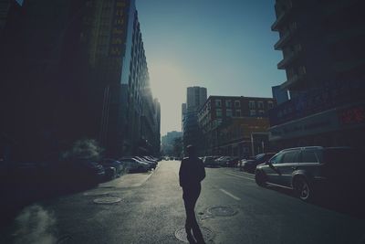 Silhouette man walking on road along buildings