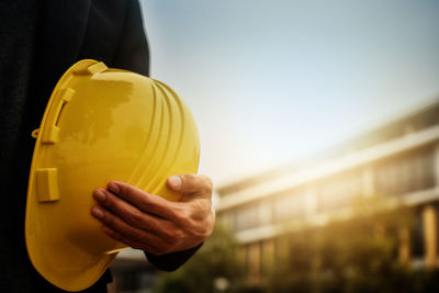 Midsection of man holding yellow umbrella against sky