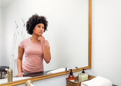 Young woman looking away while standing against wall