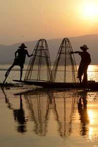 Silhouette men fishing in lake at sunset