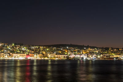 Illuminated city by sea against sky at night