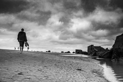 Rear view of man walking on beach against sky