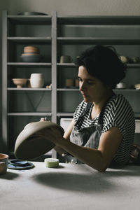 Mature craftswoman painting bowl at table in workshop