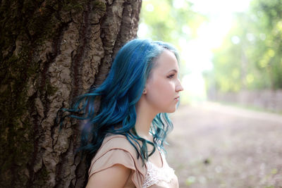 Portrait of beautiful young woman against tree trunk