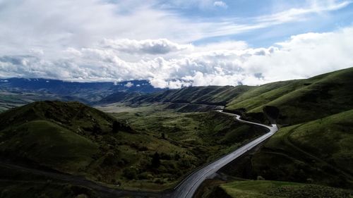 Shiny windy road along a green mountain side with a powerful cloudy sky. 