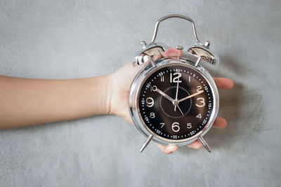 Close-up of human hand holding alarm clock against wall