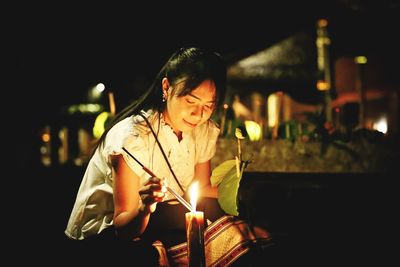 Woman igniting candle at night