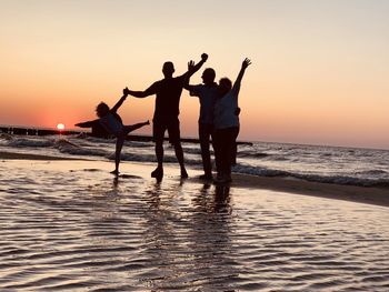 Cheerful people standing at beach during sunset