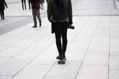 Low section of person with camera skateboarding on footpath