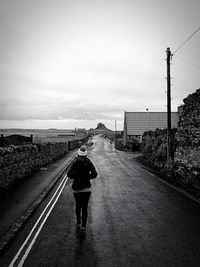 Rear view of woman walking on road against sky