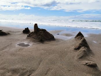 Rocks on beach against sky and sand castle 