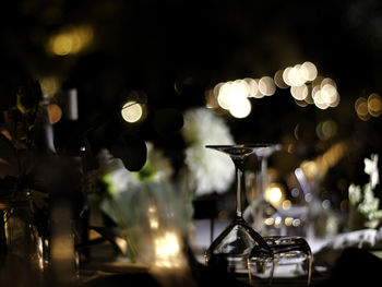 Flowers and wineglass on table against illuminated lights in restaurant